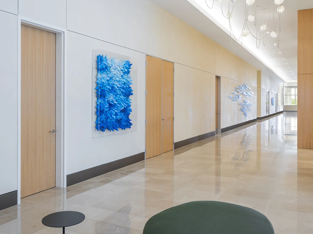 A cream and ecru office corridor with blue textural wall sculptures displayed on the wall.