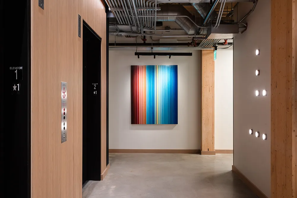 An abstract, modern painting hangs in the hallway of a modern office.