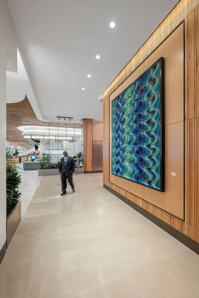 A man in a suit and tie looks up at a large piece of original, framed, abstract art on the wall in an office lobby.